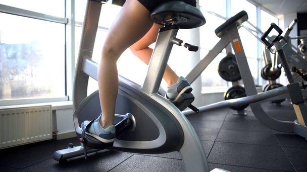 Womans legs training on stationary bike, burning calories, cardio exercise - Foto, Imagem