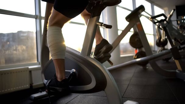Athlete male with bandaged leg riding stationary bike in morning, recovery - Foto, Imagem