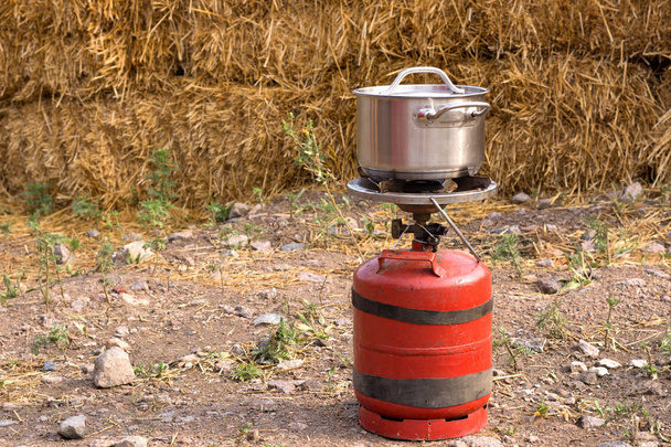 Pequeño cilindro de gas propano y almohadilla de calefacción para cocinar. Cocinar en una sartén en condiciones de campo
. - Foto, imagen