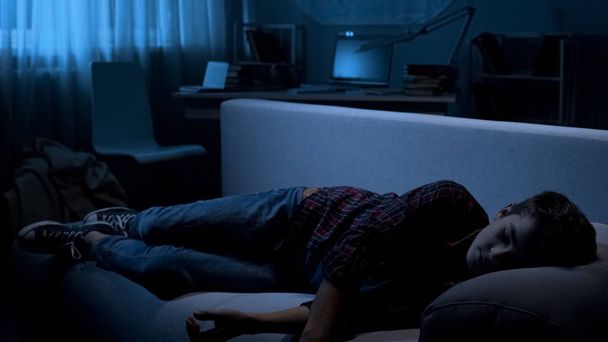 Male teen fallen asleep on couch in front of TV, free time at home, awkward age - Foto, Imagen