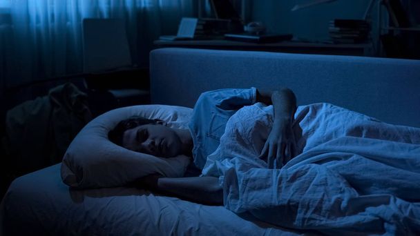 Overworked cute male student sleeping in his bed after working day at collage - 写真・画像