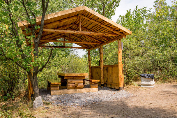 Um gazebo aberto de um tronco de árvore, bancos e uma mesa feita de tábuas, para recreação ao ar livre. Acampamento
 - Foto, Imagem