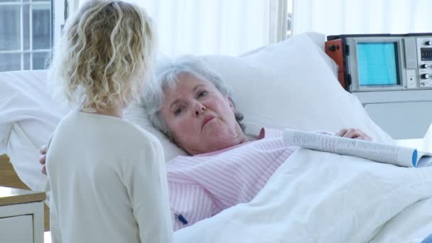 Senior woman lying in bed in hospital talking to a little girl - 映像、動画