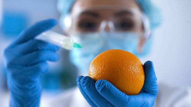 Lady biologist filling fresh orange with test substance, cosmetology research - Foto, Bild