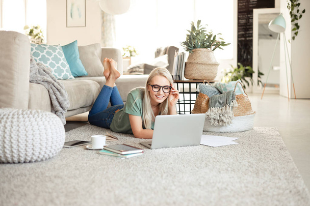 Beautiful young woman lying on the floor in living room at home and using a laptop. - Foto, Bild