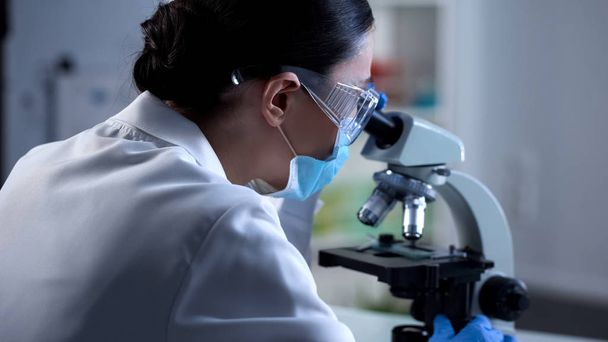Female scientist analyzing sample under microscope, microbiology research - Фото, зображення