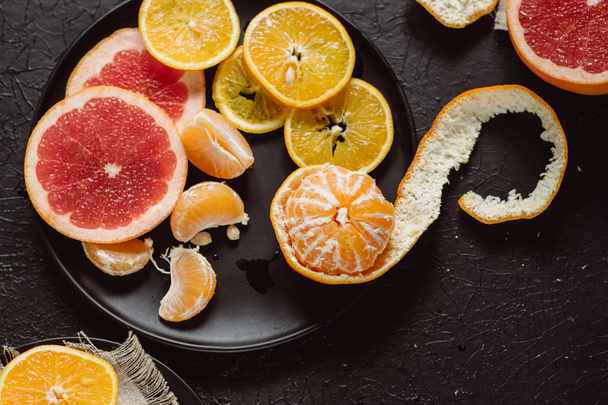 Delicious various types fresh of citrus fruit in plates on dark background - Фото, изображение