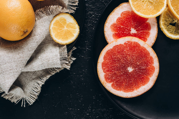 Вкусные различные виды свежих цитрусовых фруктов в тарелках на темном фоне
 - Фото, изображение