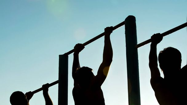 Athletic men doing pull-ups on chin-up bars, preparing for sports competition - Fotografie, Obrázek