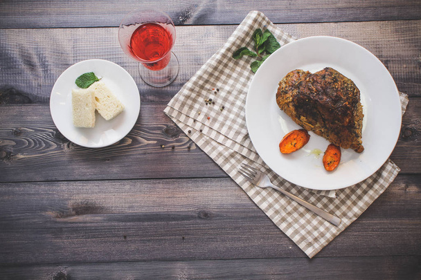 Baked meat in spices on a plate and carrots baked for a long time on a napkin on a dark gray countertop, next to a bakery tray rectangular pieces of white bread - Foto, afbeelding