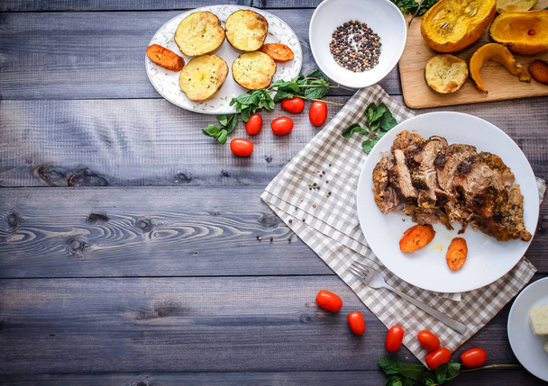 Composition of sliced meat baked in spices, carrot slices baked on a white plate on a checkered linen napkin, surrounded by cherry tomatoes, carrots baked on a plate next to potatoes; bread plate and bowl of peppers - 写真・画像
