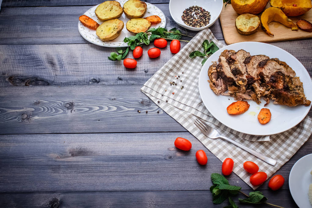 Composition of sliced meat baked in spices, carrot slices baked on a white plate on a checkered linen napkin, surrounded by cherry tomatoes, carrots baked on a plate next to potatoes; bread plate and bowl of peppers - Fotó, kép