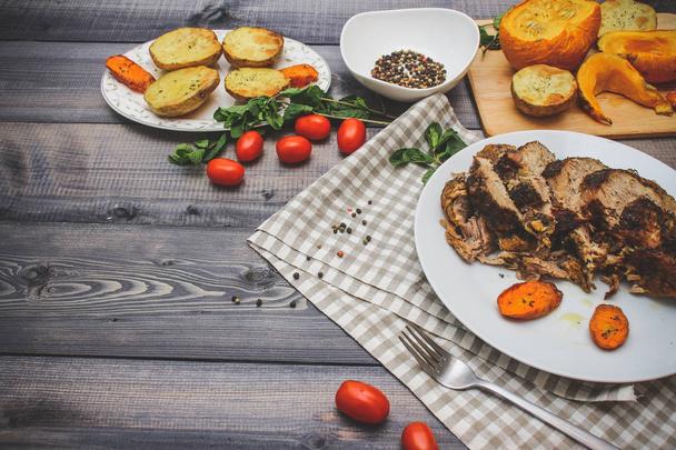 Composition of sliced meat baked in spices, carrot slices baked on a white plate on a checkered linen napkin, surrounded by cherry tomatoes, carrots baked on a plate next to potatoes; bread plate and bowl of peppers - Фото, изображение