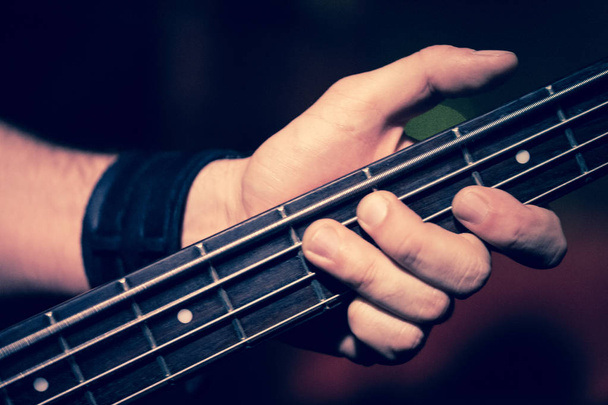 Detalhe das mãos tocando um baixo elétrico durante um concerto de música rock
 - Foto, Imagem