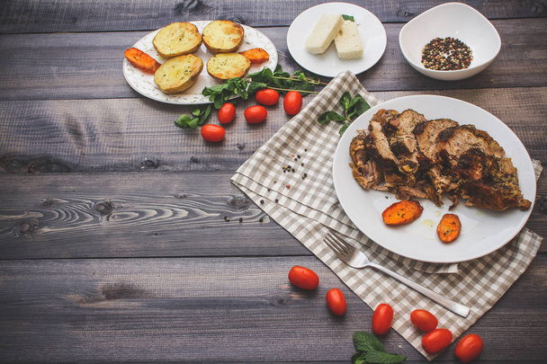 Composition of sliced meat baked in spices, carrot slices baked on a white plate on a checkered linen napkin, surrounded by cherry tomatoes, carrots baked on a plate next to potatoes; bread plate and bowl of peppers - Фото, изображение