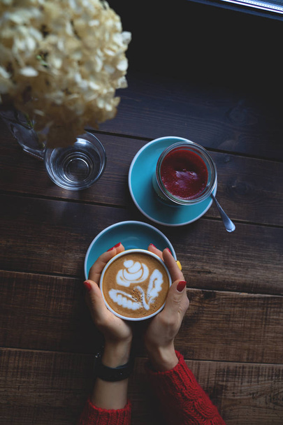 Female hands holding a Cup of coffee an dessert on wooden table - Photo, Image