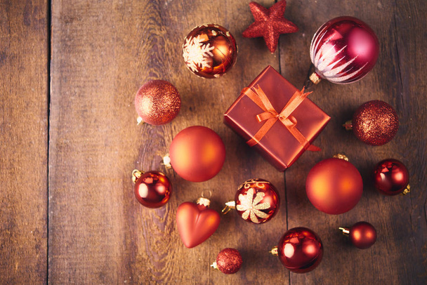 Weihnachtlicher Hintergrund. Viele rote Vintage-Kugeln, Geschenkkarton und Tannenbaum über dunklem Holzbrett. Weihnachtskonzept - Foto, Bild