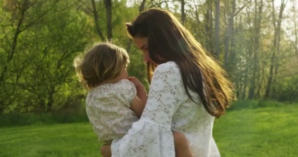 woman lifts high her adorable baby & starts turning her around smiling happiness .Happy moment parent and baby mother spending time playing with daughter in park . Medium shot of mother and baby - Кадри, відео