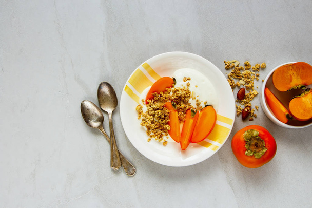 Healthy seasonal fall breakfast in plate flat lay. Granola, greek yogurt and fresh persimmon  - Photo, Image