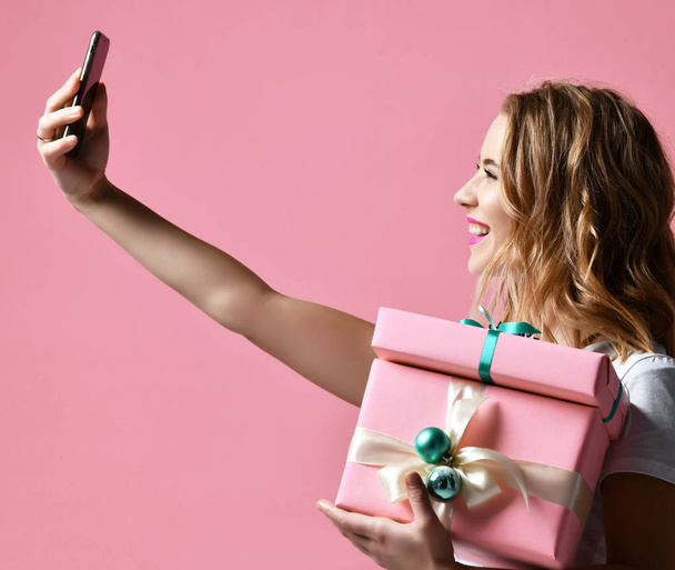 Young beautiful woman hold christmas present gifts smiling and make selfie photo with her cellphone mobile - Фото, изображение