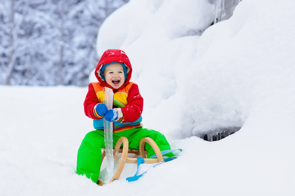 小さな男の子がそりに乗るのを楽しんでいる。子供のそり。幼児はそりに乗っている。子供たちは雪の中屋外で遊ぶ。冬にはアルプスの山々で子供たちがそります。家族のための屋外の楽しみクリスマス休暇. - 写真・画像