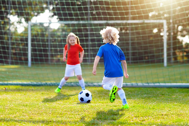 A gyerekek a szabadtéri pályán fociznak. A gyerekek gólt rúgnak a focimeccsen. Lány és fiú rúgja a labdát. Futó gyerek mezben és stopliban. Iskolai foci klub. Sportoktatás fiatal játékosok számára. - Fotó, kép