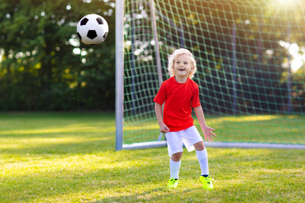 子供たちは野外でサッカーをする。子供たちはサッカーの試合でゴールを決めた。少年はボールを蹴った。チームジャージとクリートで子供を走らせている。サッカー部所属。若い選手のためのスポーツトレーニング. - 写真・画像