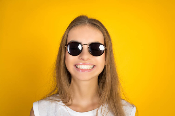 Beautiful young woman in sunglasses smiling isolated on yellow background - Fotoğraf, Görsel