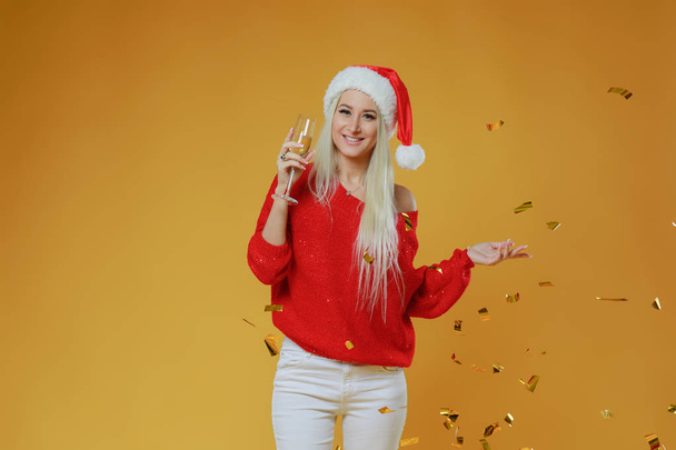 Happy excited young blond woman in santa claus hat with gift box over yellow background - Фото, зображення