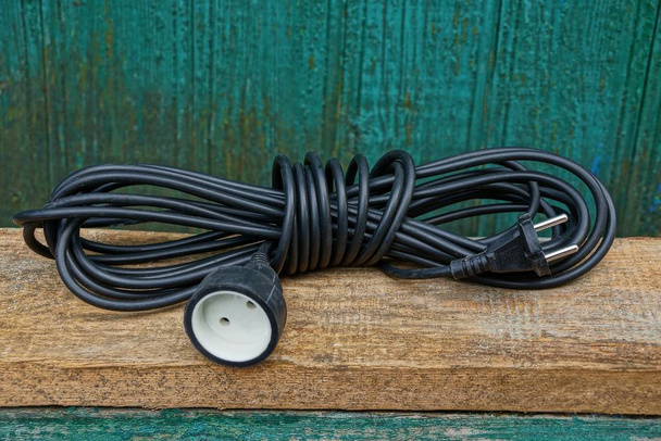 černá prodlužovací kabel v přadeno leží na hnědé dřevěné desce zelená zeď - Fotografie, Obrázek