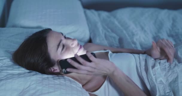 video of brunette woman lying in bed and talking on smartphone - Filmati, video