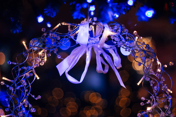 white bow on a Christmas wreath of metal wires and transparent beads on the background of light from the garlands - Foto, Imagem