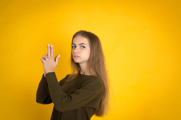 Beautiful woman in sweater is hiding hand raised and blowing at finger gun - Foto, immagini