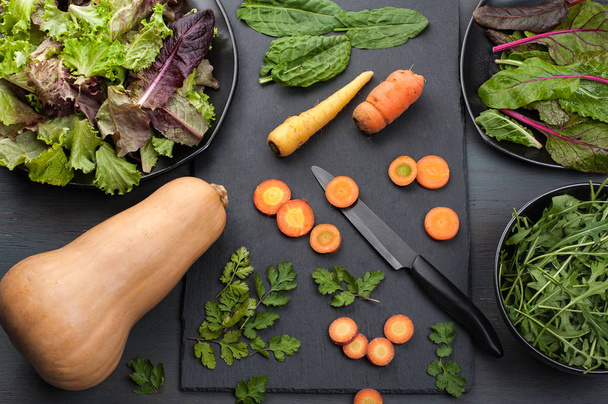Масляний кабачок, морква, змішана листяна зелень, кінза і щавлю на кухонній сцені з темним фоном
. - Фото, зображення
