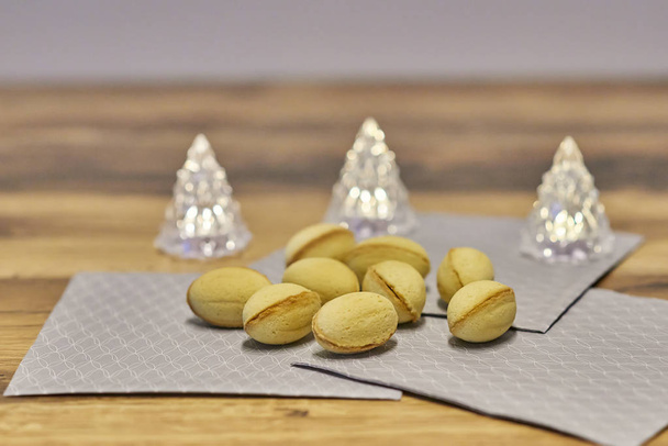 Fistful de biscoitos de manteiga em forma de noz em guardanapos cinzentos, três lâmpadas de árvore de Natal no fundo
 - Foto, Imagem