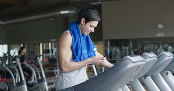 slow motion video of caucasian man on treadmill with blue towel on shoulders and using mobile phone   - Záběry, video