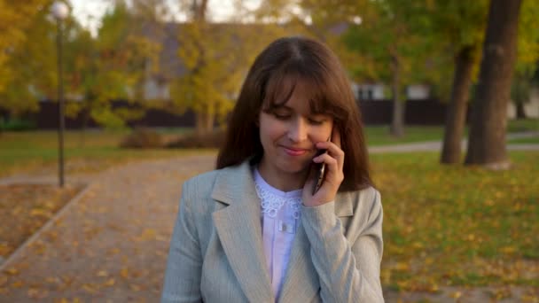 Nuori kaunis nainen puhuu matkapuhelimella puistossa, onnellinen tyttö hymyilee
. - Materiaali, video