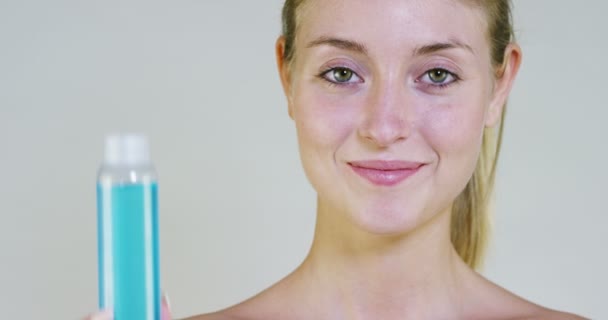 Portrait of a beautiful young girl smiling and looking at the camera, without makeup, holding lotion, on a white background. Concept:natural beauty, youth, skin care, always young, love yourself. - Záběry, video