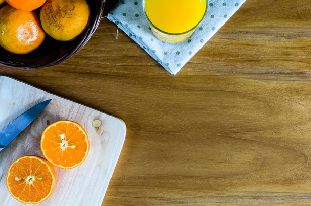 Viipaloitu appelsiini veitsellä puupalikolla ja lähellä paljon appelsiinia pajukorissa puupöydällä
. - Valokuva, kuva