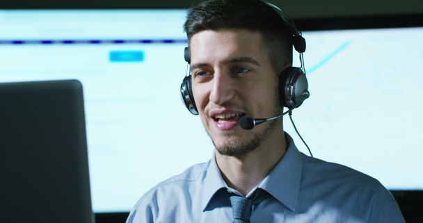ein junger Mann, der im Kundenservice oder in einem Flughafen-Kontrollturm arbeitet, nimmt Anrufe von Telefonkunden Tag und Nacht mit einem Lächeln entgegen. - Filmmaterial, Video