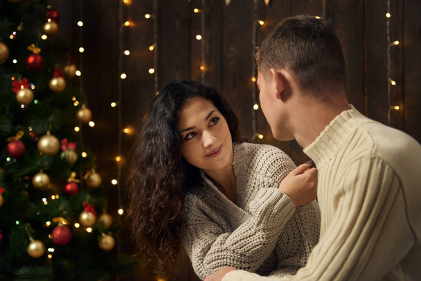young couple in christmas lights and decoration, dressed in white, fir tree on dark wooden background, winter holiday concept - Φωτογραφία, εικόνα
