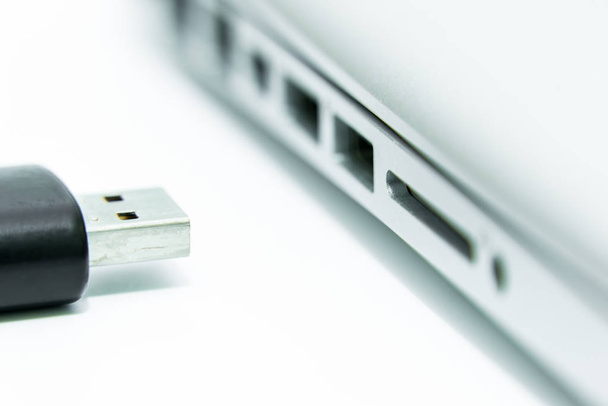 Μαύρο USB που είναι συνδεδεμένο στη θύρα USB του φορητού υπολογιστή για αντιγραφή και μεταφορά δεδομένων σε απομονωμένο και λευκό φόντο. - Φωτογραφία, εικόνα