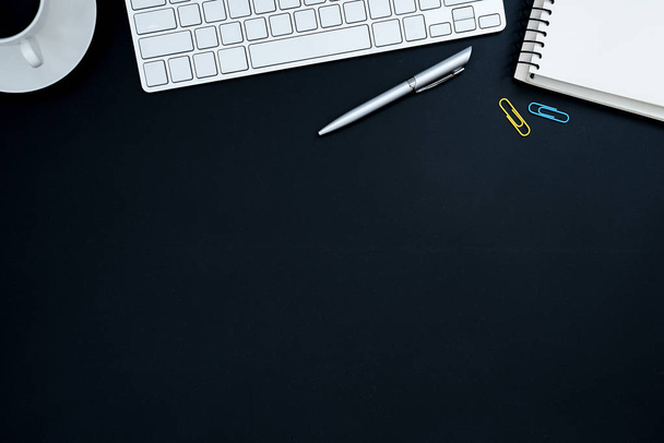 Mesa de escritório com computador, caneta de prata, clipe de papel azul e amarelo e xícara de café preto. Mesa de mesa de negócios vista superior com conceito de espaço de cópia
. - Foto, Imagem