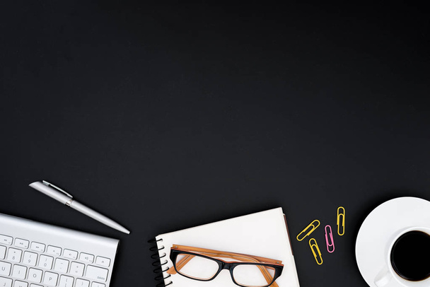 Schreibtisch mit Computer, Brille, silbernem Stift, rosa und gelben Büroklammer und schwarzer Kaffeetasse. Business-Tisch-Ansicht mit Kopierraum-Konzept. - Foto, Bild