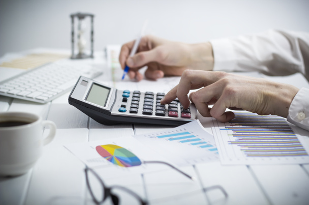 Podnikatel, účetní, píše zprávu pomocí kalkulačky, zatímco sedí za stolem v kanceláři. - Fotografie, Obrázek