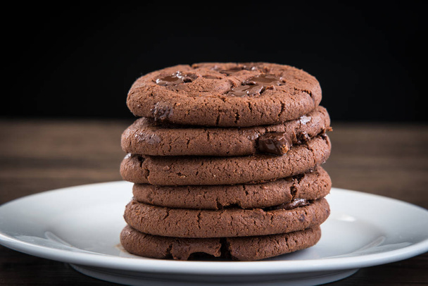Biscuits au chocolat noir sur plaque blanche et table en bois
. - Photo, image