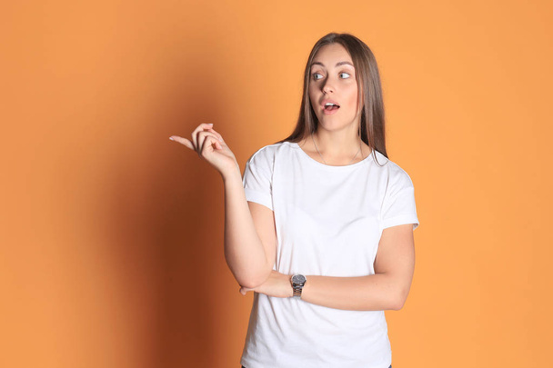 Young woman in basic clothing smiling and pointing finger at copyspace isolated on yellow background. - Photo, Image