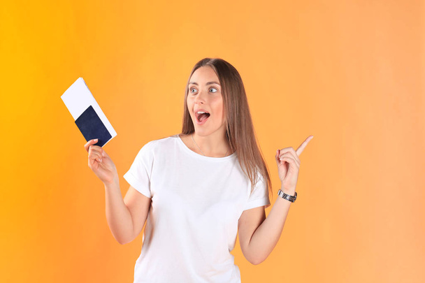 Excited young woman tourist standing isolated on yellow background holding passport with tickets. - Fotoğraf, Görsel