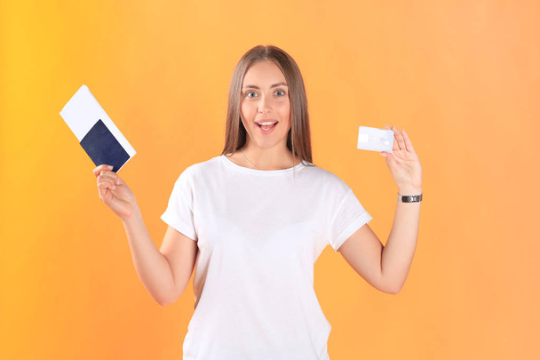 Excited young woman tourist standing isolated on yellow background holding passport with tickets, plastic credit card. - 写真・画像