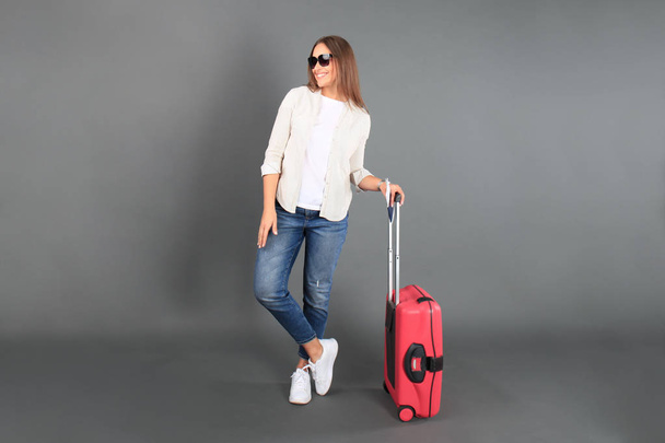 Young tourist girl in summer casual clothes, with sunglasses, red suitcase, passport, tickets isolated grey background. - 写真・画像